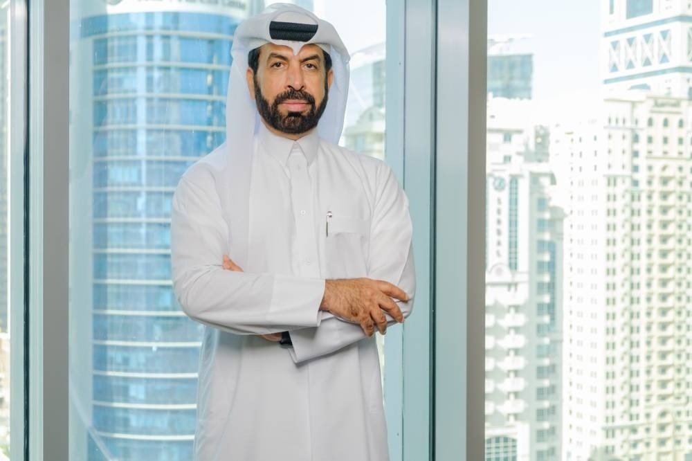 Aamal Company Chief Executive Rashid bin Ali Al Mansoori stands with arms folded beside a window overlooking Doha towers