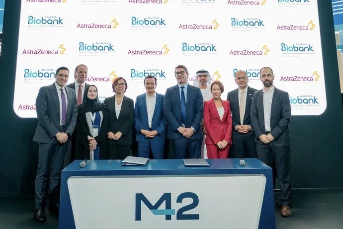 A group of men and women in business attire stand behind a podium marked M42 in front of a backdrop with Abu Dhabi Biobank and AstraZeneca logos