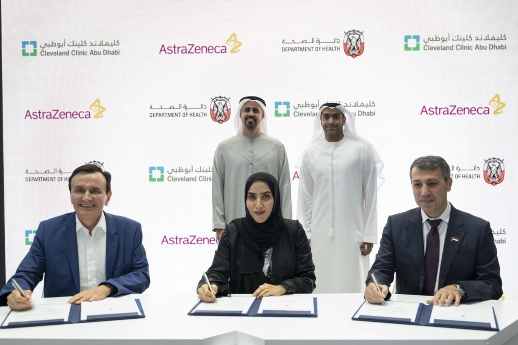 Three officials sign agreements at a table in front of AstraZeneca, Cleveland Clinic Abu Dhabi and Department of Health backdrops as two men stand behind