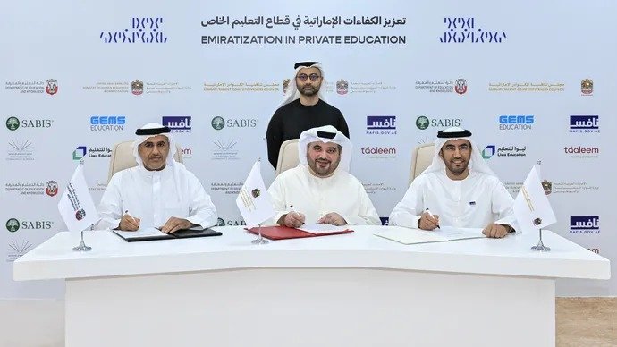 Three officials in Emirati dress sign documents at a table in front of a backdrop reading Emiratization in Private Education, with a fourth man standing behind them