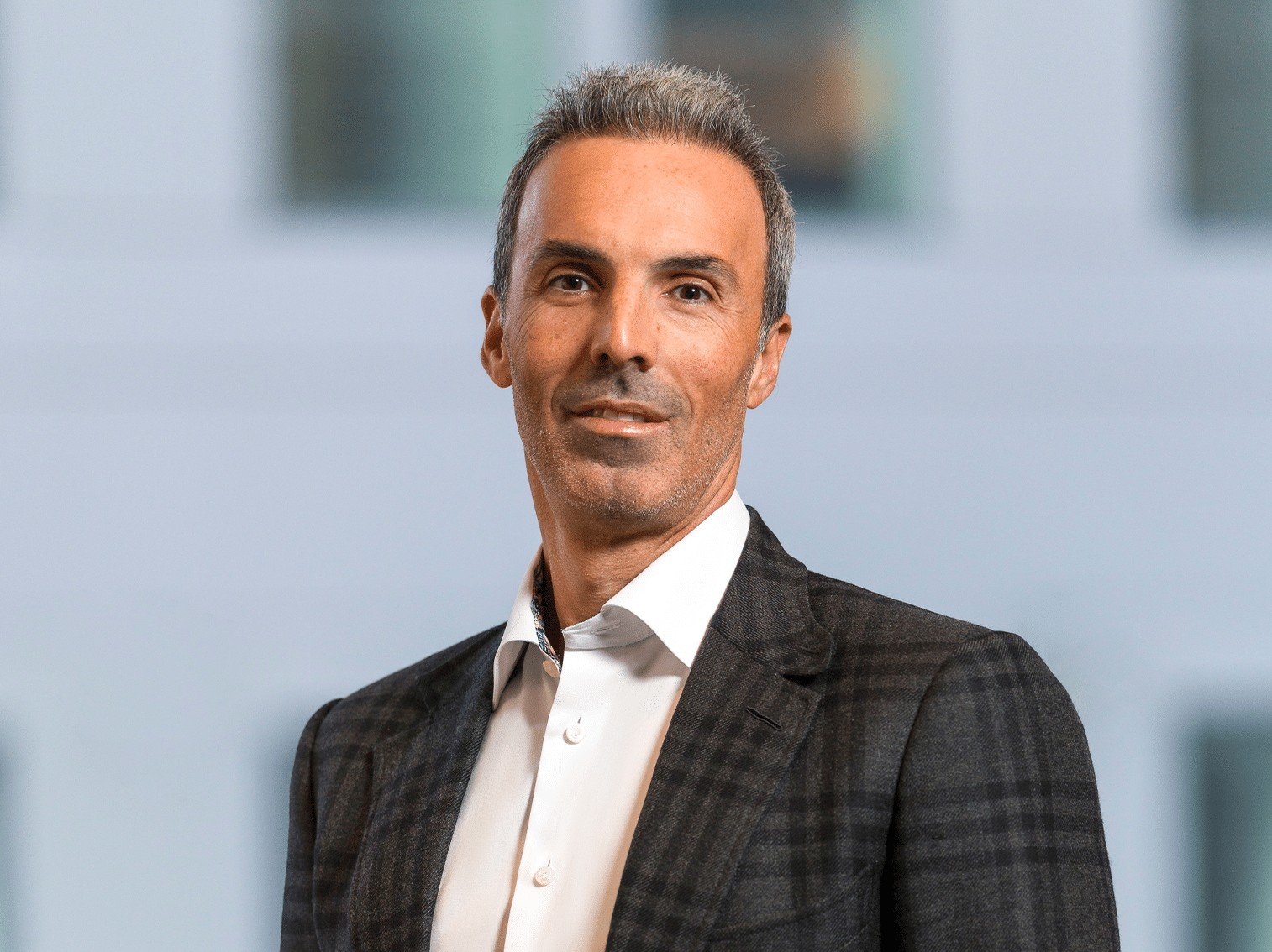 Portrait of Mehdi Iraqi of private equity firm Advent, wearing a dark checked jacket and white shirt