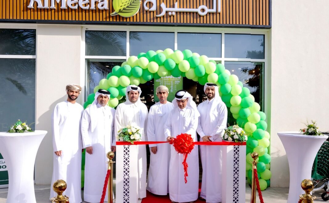 Men in traditional Qatari dress stand at a ribbon-cutting outside a new Al Meera supermarket decorated with green balloons