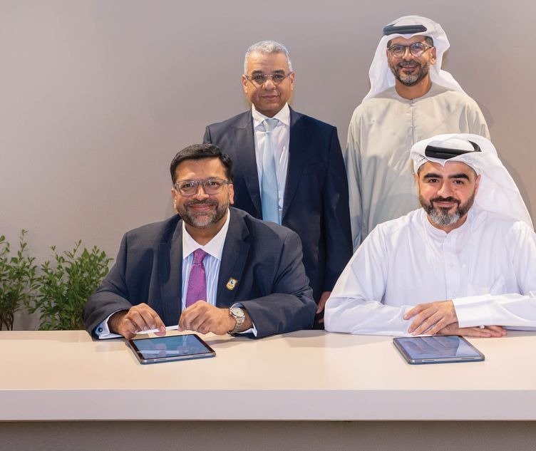 Two executives seated at a white table with tablets and two others standing behind them at the Aldar and ADIB card launch