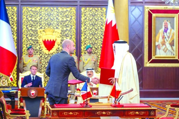 Jean-Noel Barrot and Abdullatif Al Zayani shake hands at a signing table as Emmanuel Macron and King Hamad watch