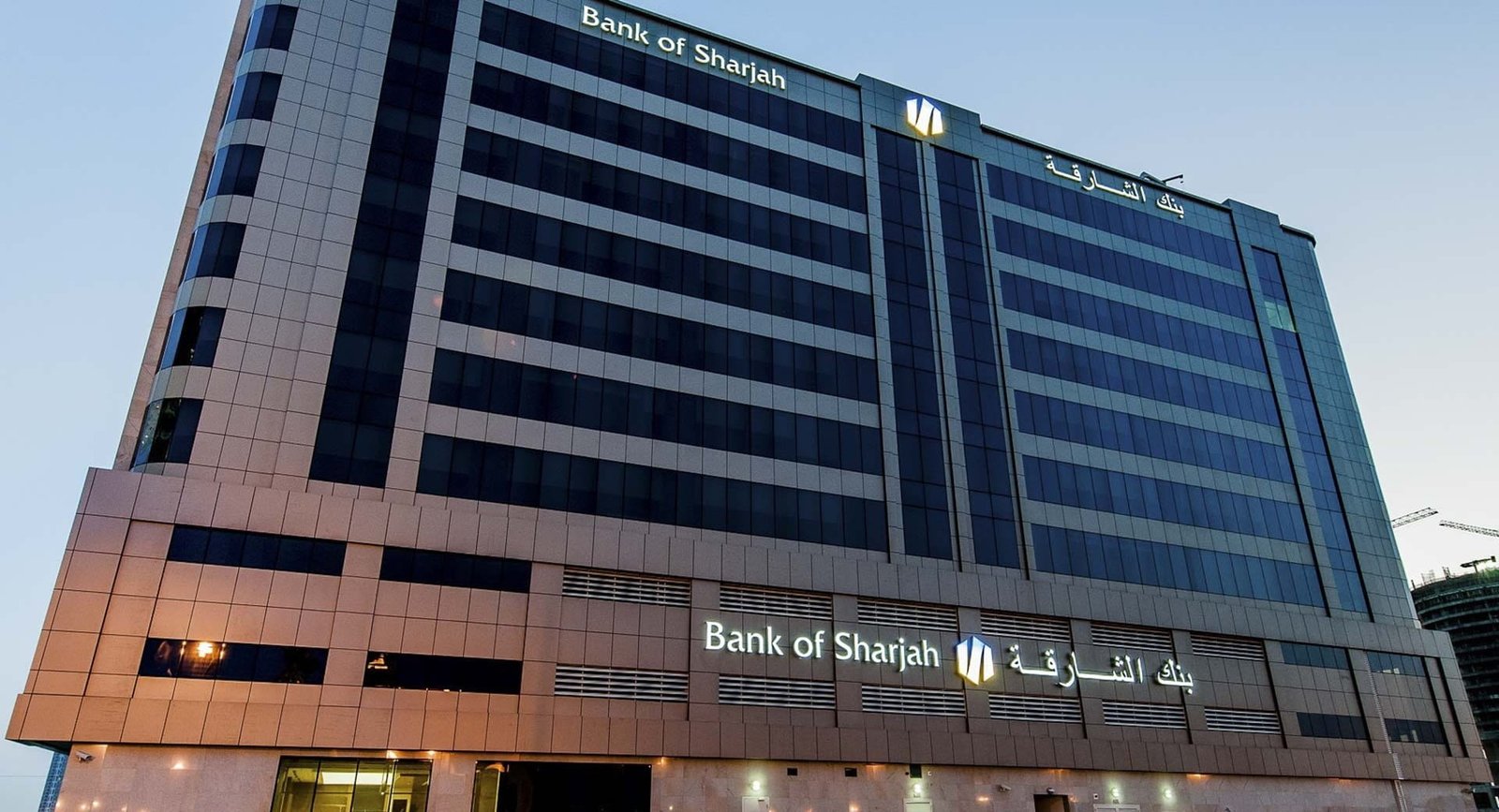 Bank of Sharjah headquarters tower in Sharjah at dusk with the bank's name lit on the facade