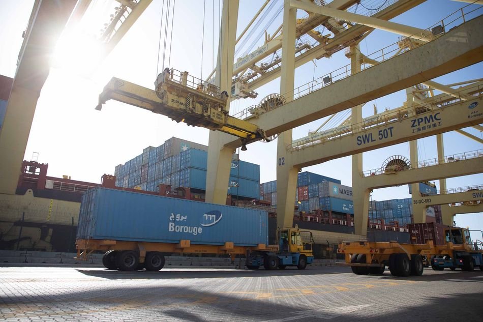 A Borouge shipping container on a trailer beneath gantry cranes at a container port