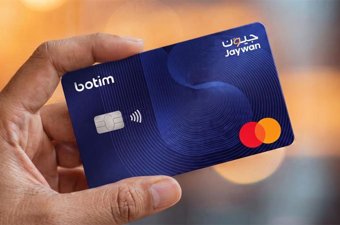A hand holds a dark blue Botim One prepaid card bearing the Jaywan national card scheme mark