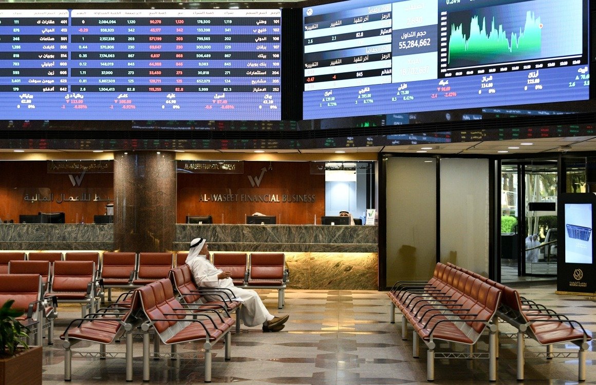 An investor sits beneath market screens in the Boursa Kuwait trading hall