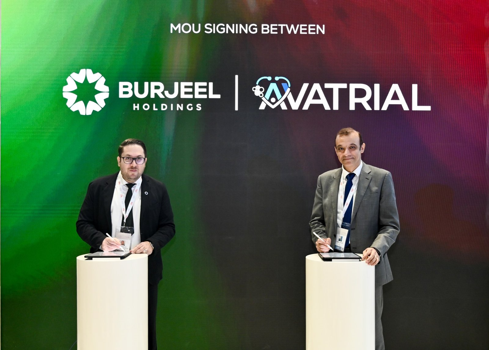 Two men in suits sign documents on tablets at white podiums in front of a screen reading MoU signing between Burjeel Holdings and Avatrial