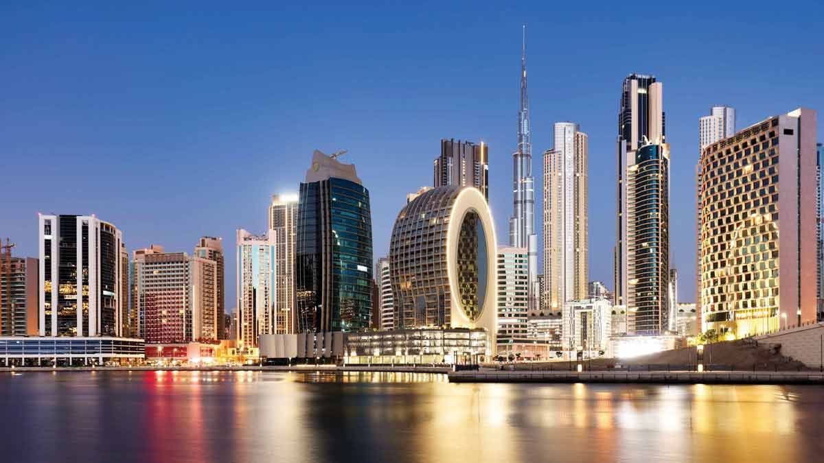 Towers in Business Bay along the Dubai Water Canal at dusk, with Burj Khalifa behind