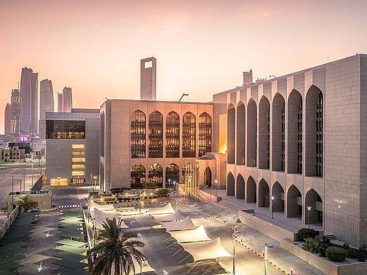 Headquarters of the Central Bank of the UAE in Abu Dhabi at dusk, with arched facades and the city skyline behind