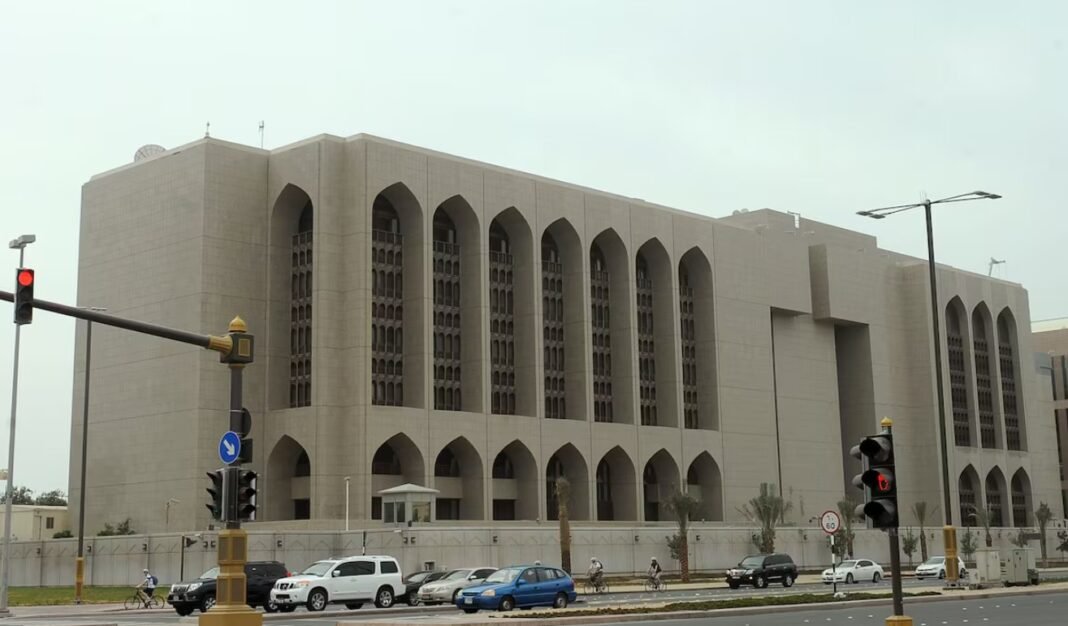 The stone facade of the Central Bank of the UAE headquarters in Abu Dhabi, with arched windows, seen from a road with traffic lights