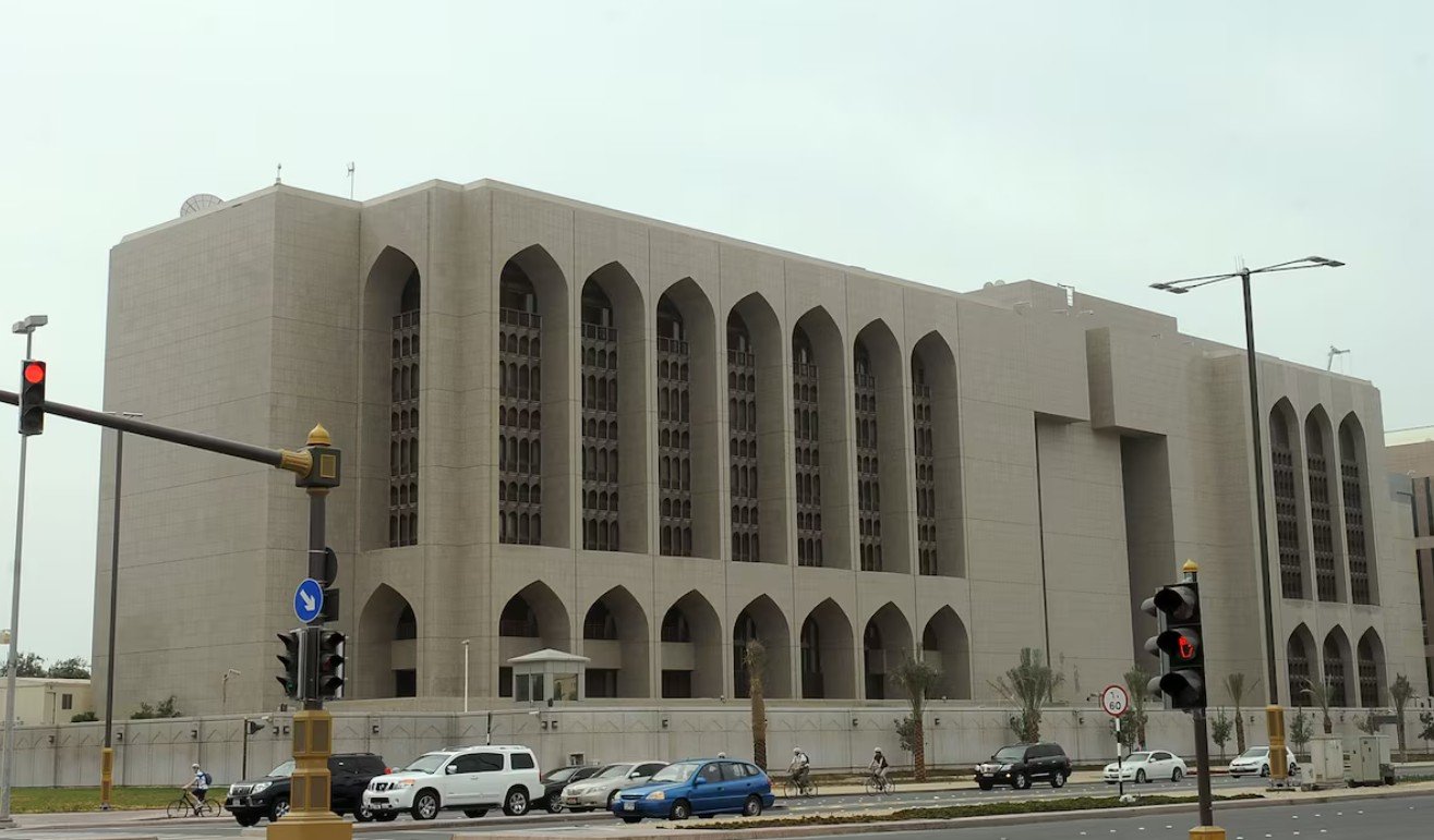 The stone facade of the Central Bank of the UAE headquarters in Abu Dhabi, with arched windows, seen from a road with traffic lights