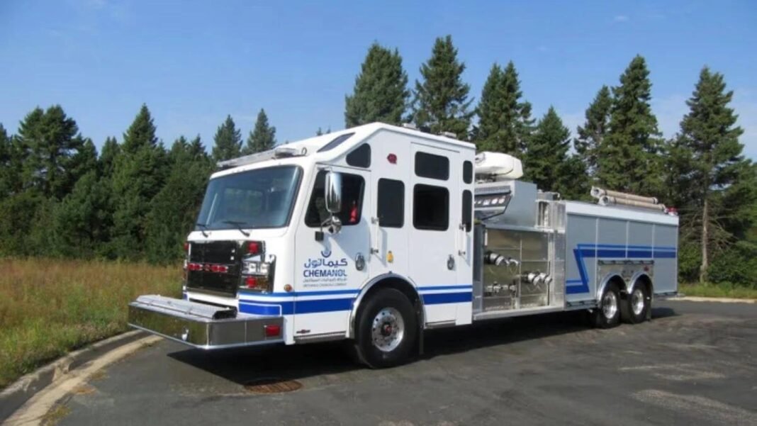 A white fire truck carrying the Chemanol logo parked on a road in front of pine trees