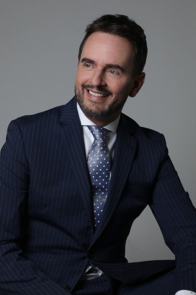 Portrait of a smiling man with a beard wearing a dark pinstripe suit and tie