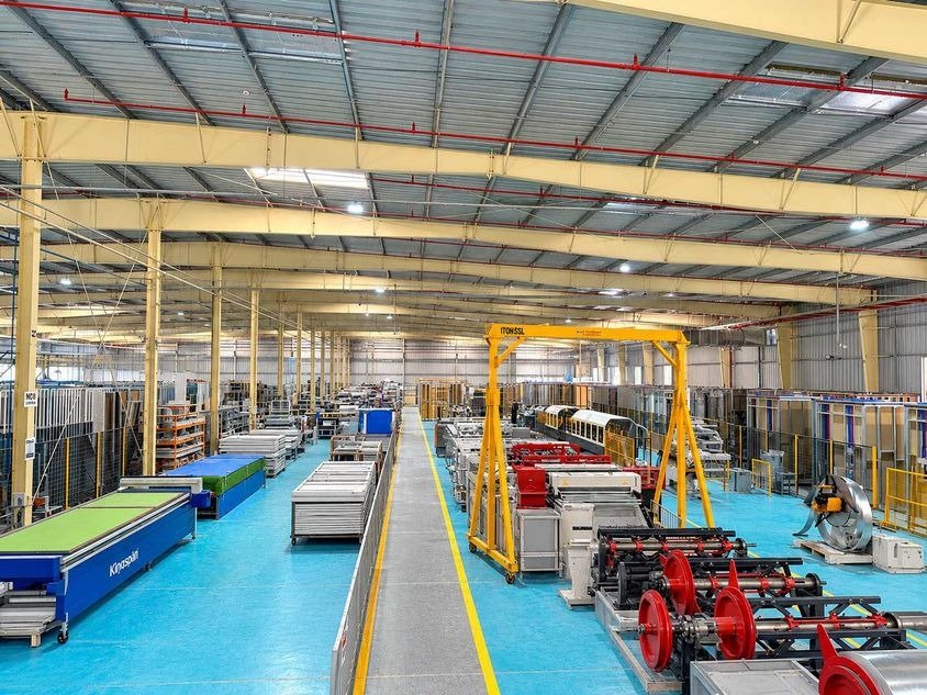 Factory floor with yellow gantry crane, panel production tables and machinery under a high steel roof