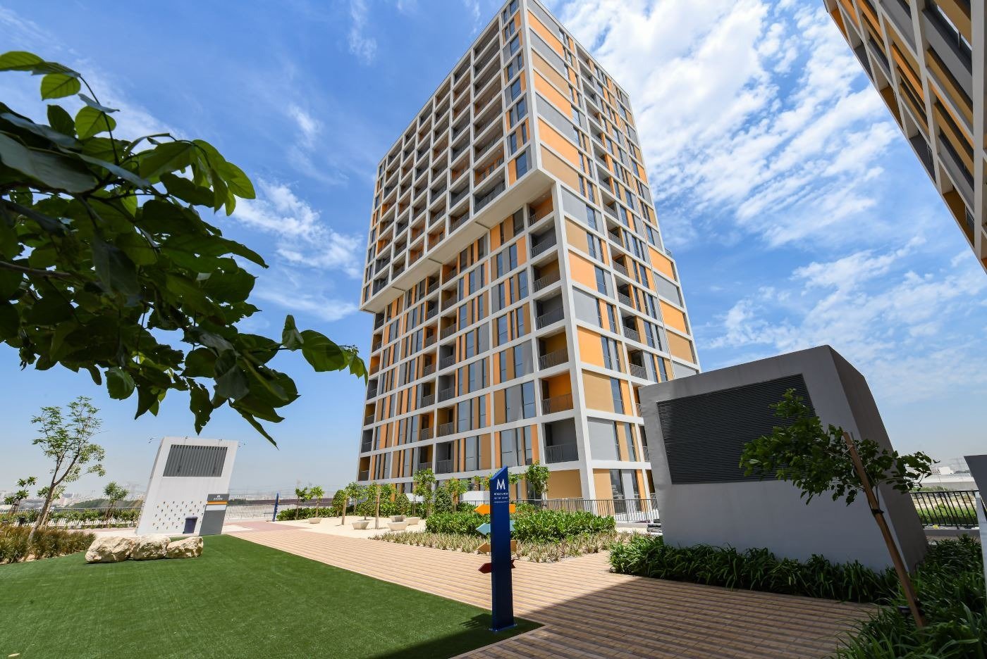 Residential tower with orange and white facade and landscaped gardens at Deyaar's Midtown community in Dubai