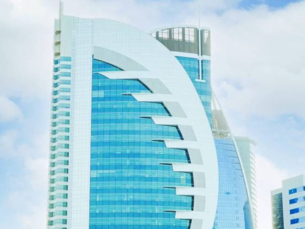 Doha Bank's curved glass headquarters tower in Doha's West Bay district under a cloudy sky