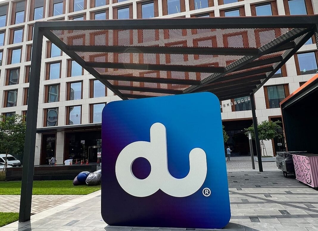A large blue and purple du logo sign beneath a steel canopy in front of an office building