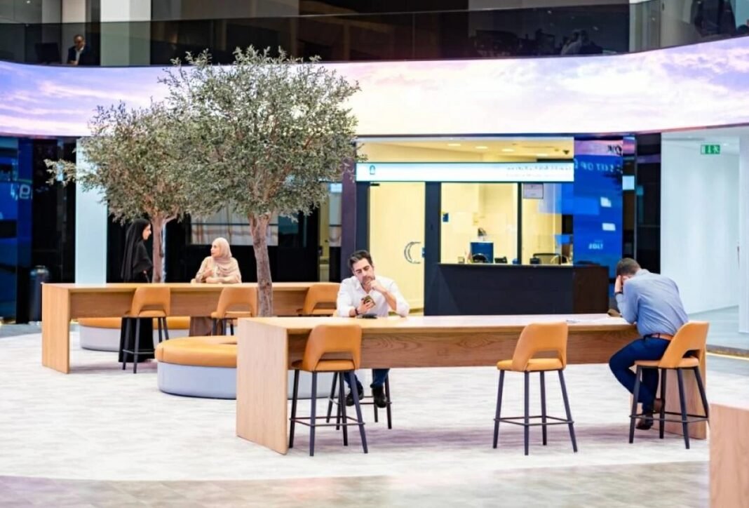 Investors sit at wooden tables with orange stools in the open trading hall of the Dubai Financial Market