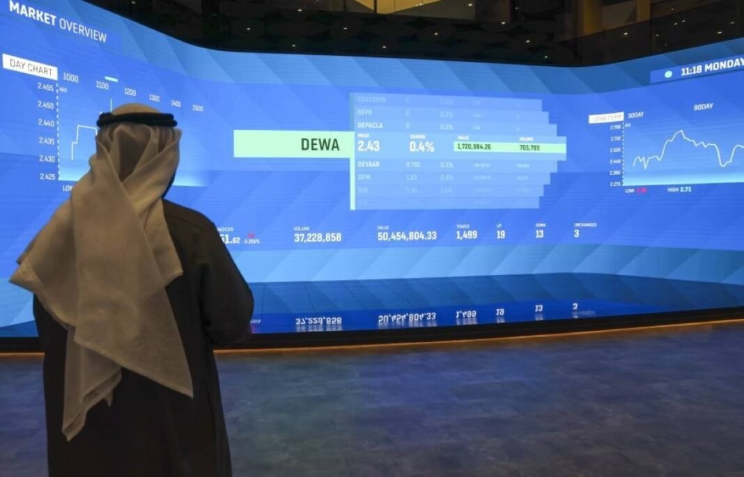 Man in traditional Emirati dress standing before a large blue market display screen at the Dubai Financial Market