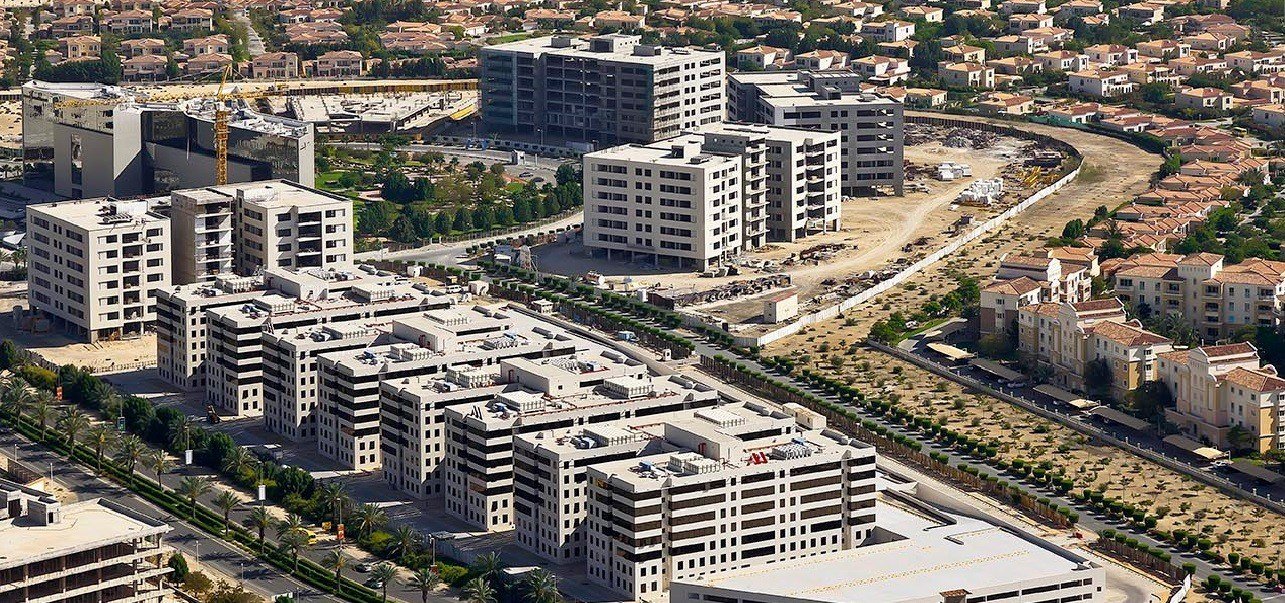 Aerial view of mid-rise office and residential buildings, tree-lined roads and villas in Dubai Investments Park