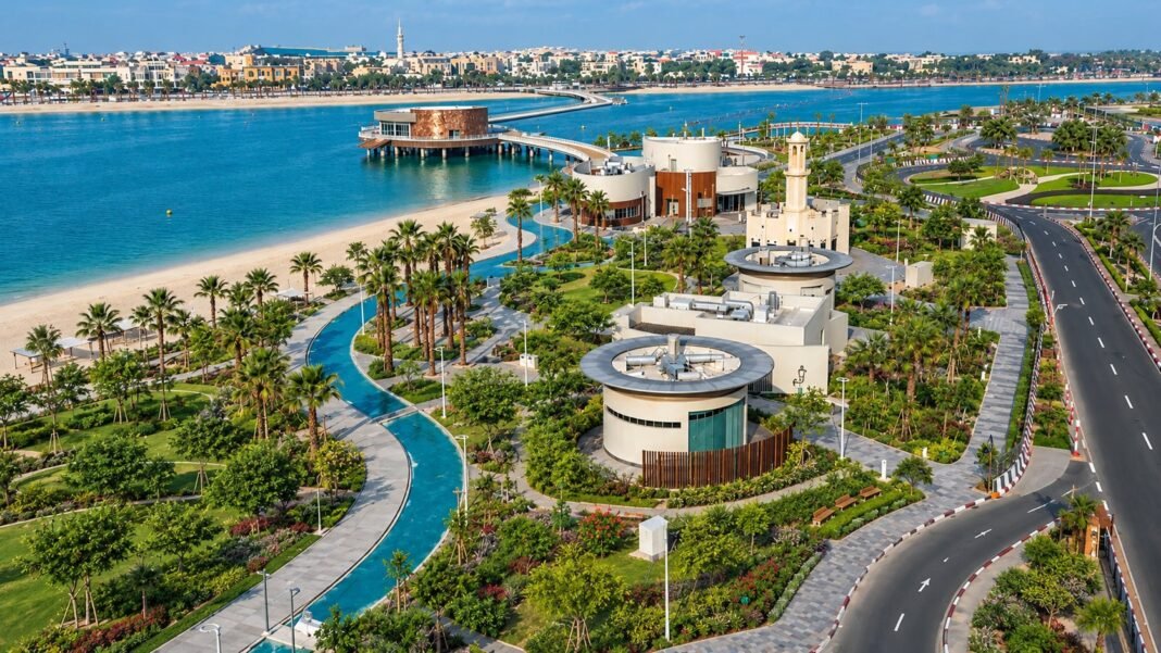 Aerial view of a landscaped beachfront park with walkways, palm trees and a water channel in Dubai