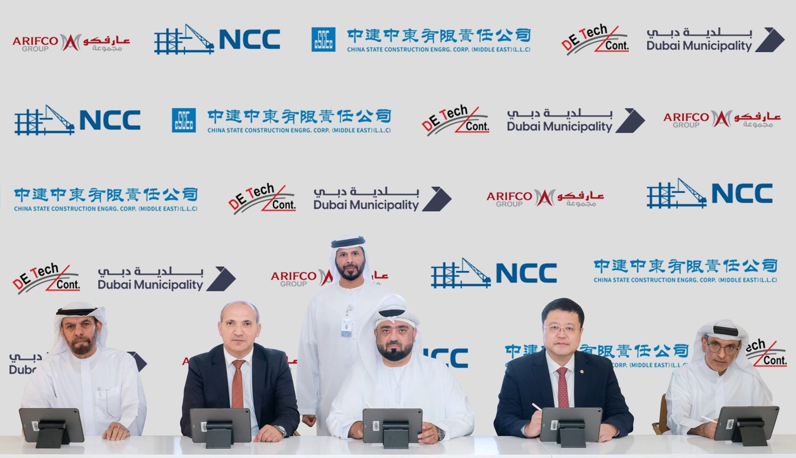 Officials sit at a signing table in front of a backdrop with the logos of Dubai Municipality and contractors for the Tasreef program