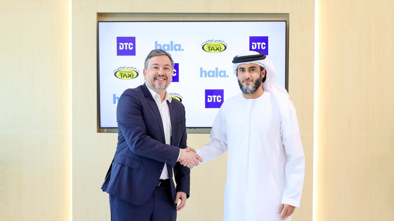 Two executives shake hands in front of a screen showing the DTC, Hala and National Taxi logos