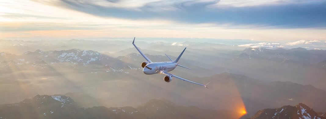 A flydubai Boeing 737 MAX in white livery flying above a mountain range at sunset