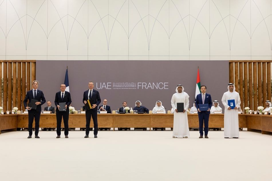 Officials stand holding signed agreement folders in front of a UAE France Business Dialogue backdrop in Abu Dhabi