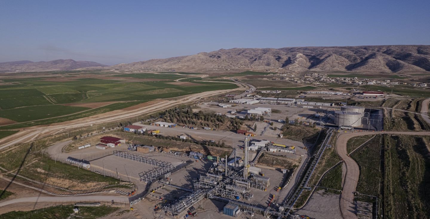 Aerial view of an oil production facility with storage tanks and pipework surrounded by farmland and hills in Iraq's Kurdistan Region