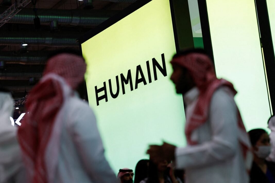 Men in red-checked headdresses walk past a large illuminated Humain sign at an exhibition stand