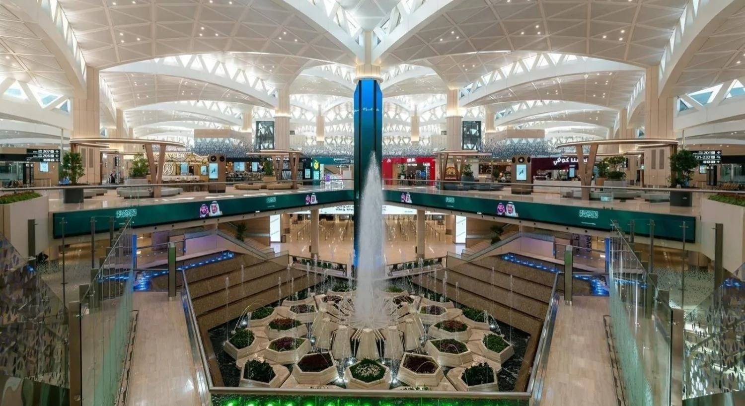 Interior of a passenger terminal at King Khalid International Airport in Riyadh, with a central fountain, planters and a white vaulted ceiling