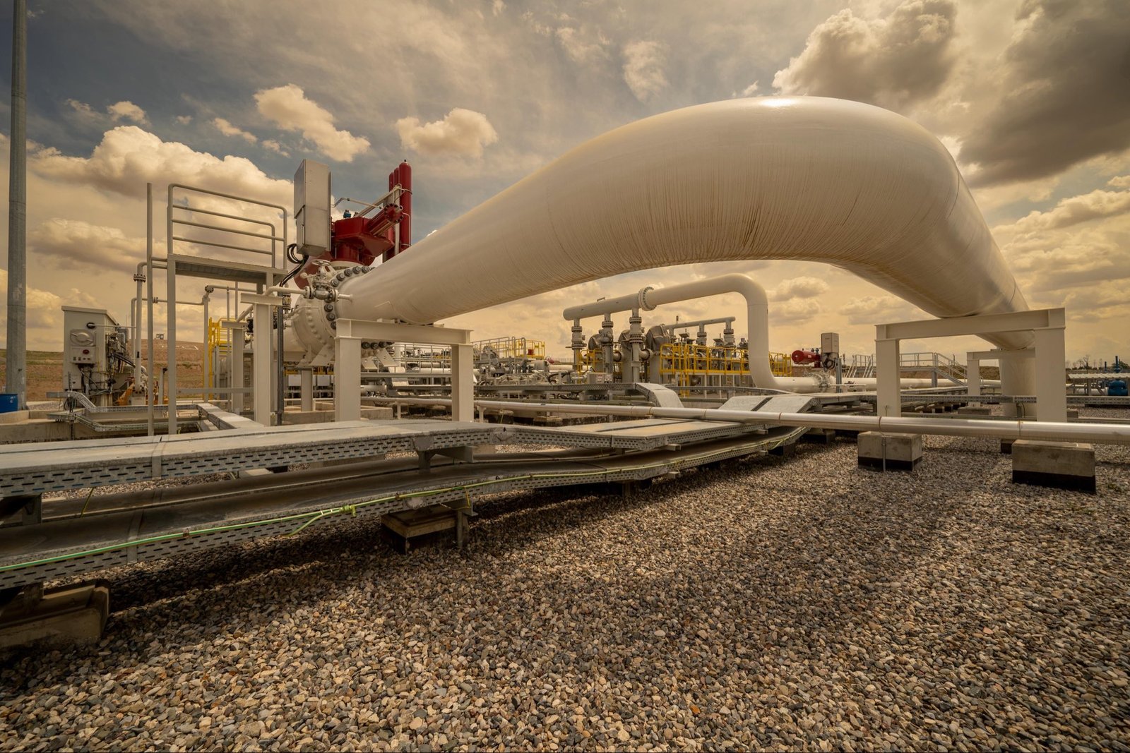 White pipelines and valves at an energy facility under a cloudy sky