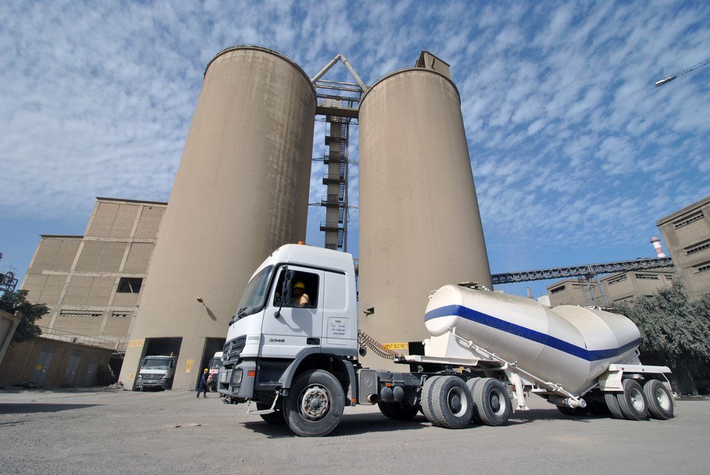 A cement tanker truck in front of storage silos at a Kuwait Cement Company plant