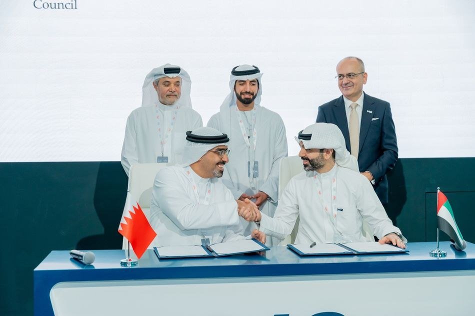 Two men in white robes shake hands at a signing table with Bahraini and UAE flags as three men stand behind them
