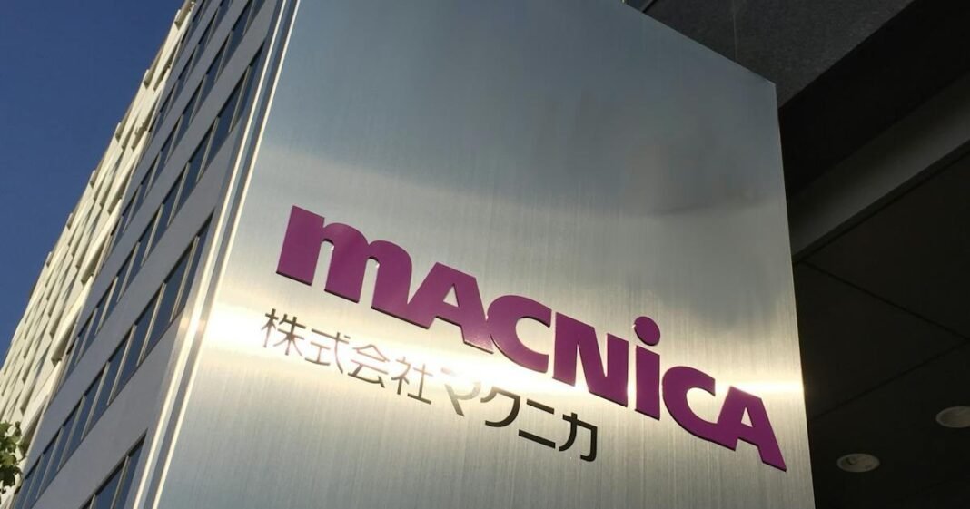 A brushed steel sign with the purple Macnica logo and Japanese characters outside an office building