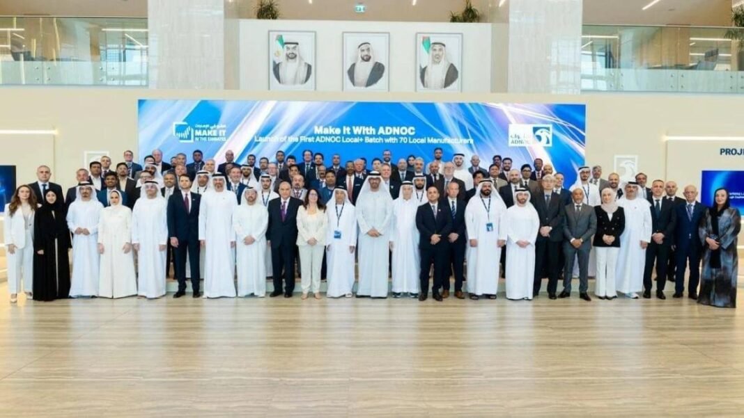 A large group of men and women in business attire and traditional Emirati dress pose in front of a Make It With ADNOC screen