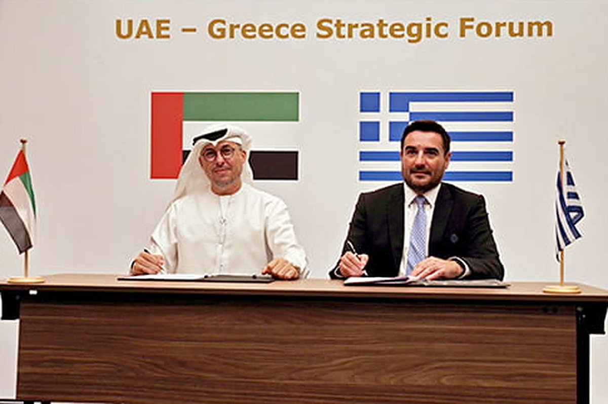 Two officials sign documents at a table in front of UAE and Greek flags under a UAE-Greece Strategic Forum banner