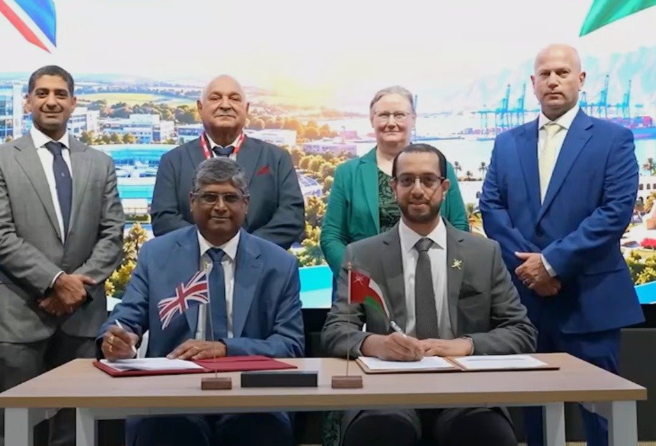 Executives sign an agreement between Mohammed Al Barwani Satellite Company and ST Engineering iDirect at a table with British and Omani flags
