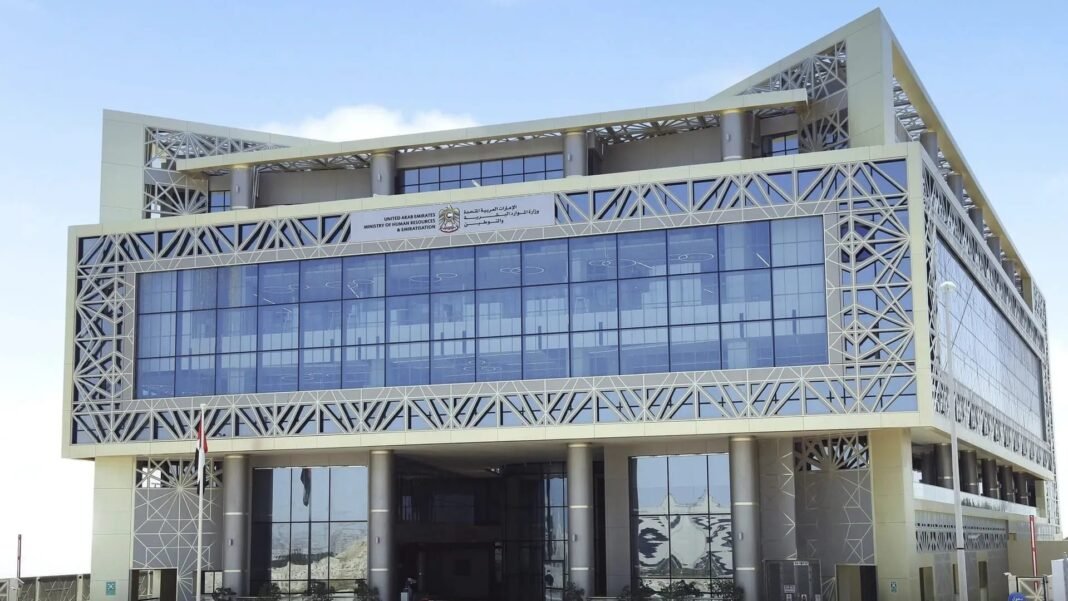 The glass and latticework facade of a Ministry of Human Resources and Emiratisation building in the UAE, with a UAE flag outside