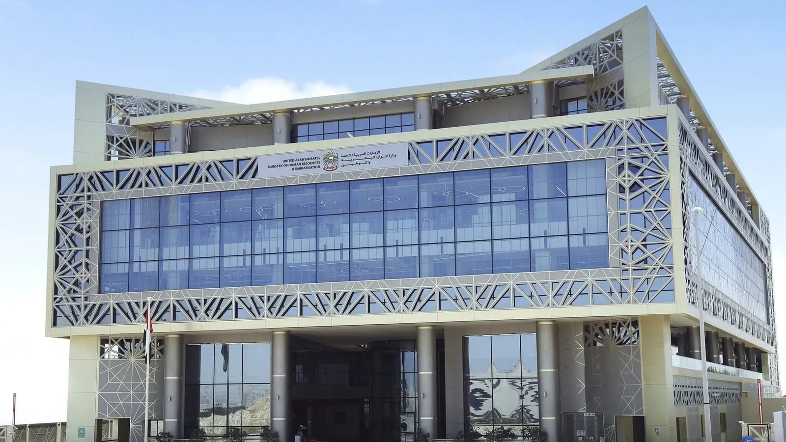 The glass and latticework facade of a Ministry of Human Resources and Emiratisation building in the UAE, with a UAE flag outside
