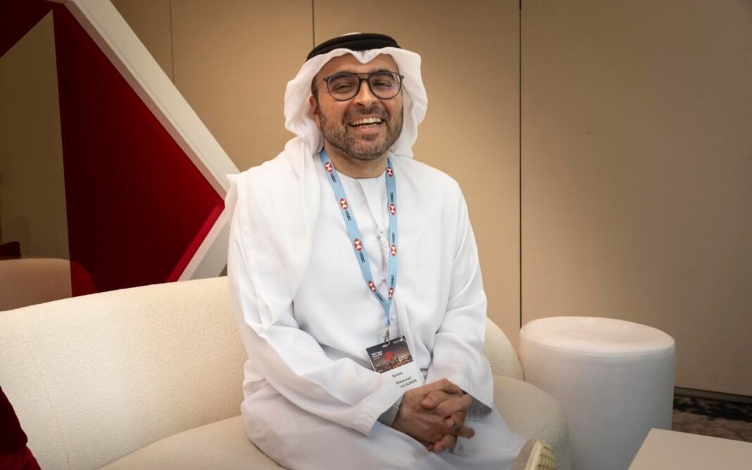 Mohammad Abdulrahman Alhawi, wearing a white kandura and an event lanyard, smiles while seated on a cream sofa