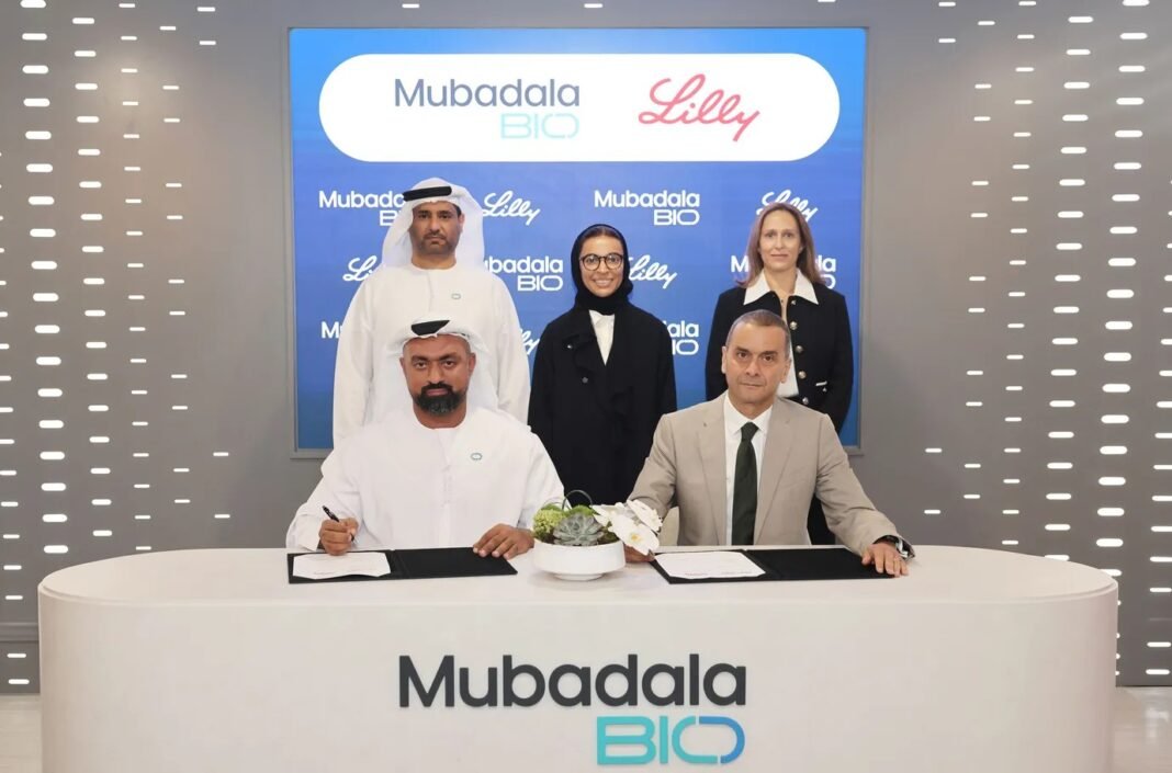Mubadala Bio and Eli Lilly executives sign an agreement at a table in front of a Mubadala Bio and Lilly backdrop