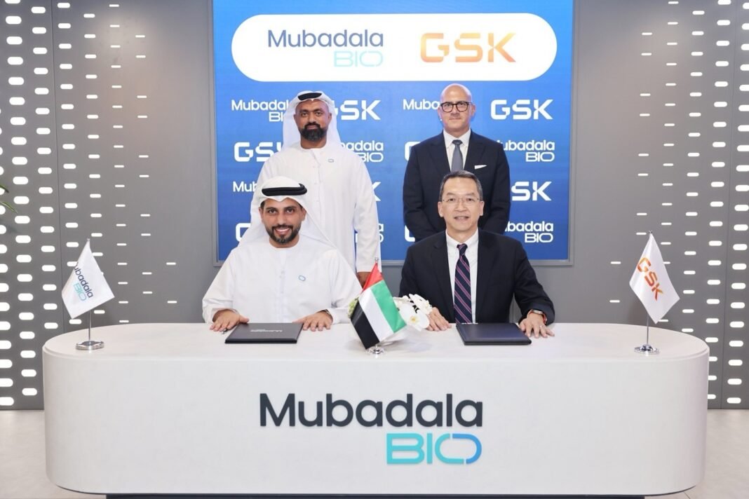 Two executives sign documents at a white Mubadala Bio desk as two colleagues stand behind them in front of a Mubadala Bio and GSK backdrop