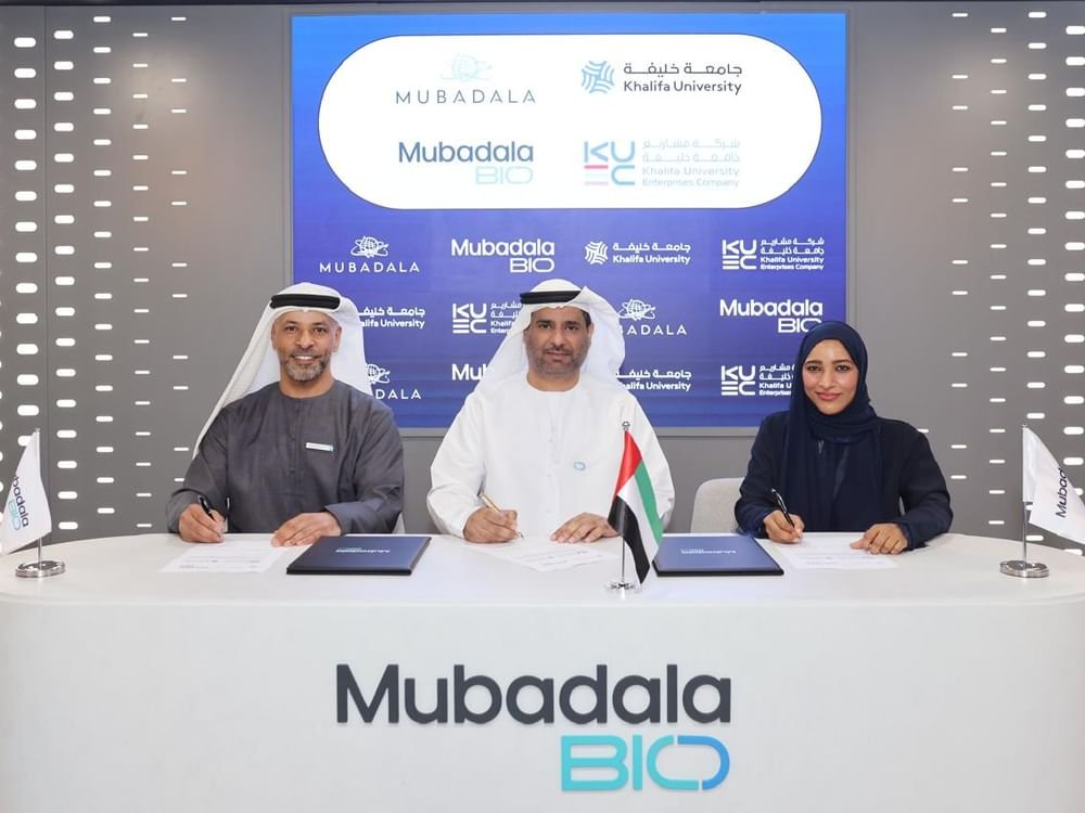 Three executives signing documents at a table in front of Mubadala, Mubadala Bio and Khalifa University logos