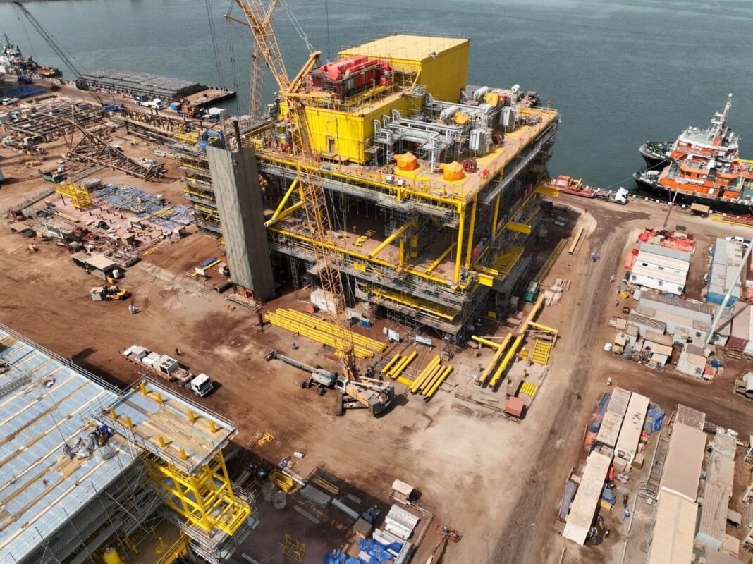 Aerial view of a large yellow offshore platform topside under construction at a fabrication yard beside the sea