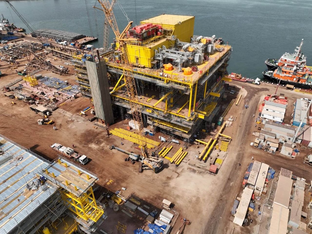 Aerial view of a large yellow offshore platform topside under construction at a fabrication yard beside the sea