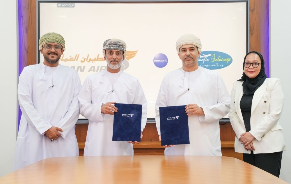 Four people, three men in white Omani dress and a woman in a white blazer, stand in front of a screen showing the Oman Air logo, two of them holding blue signed folders
